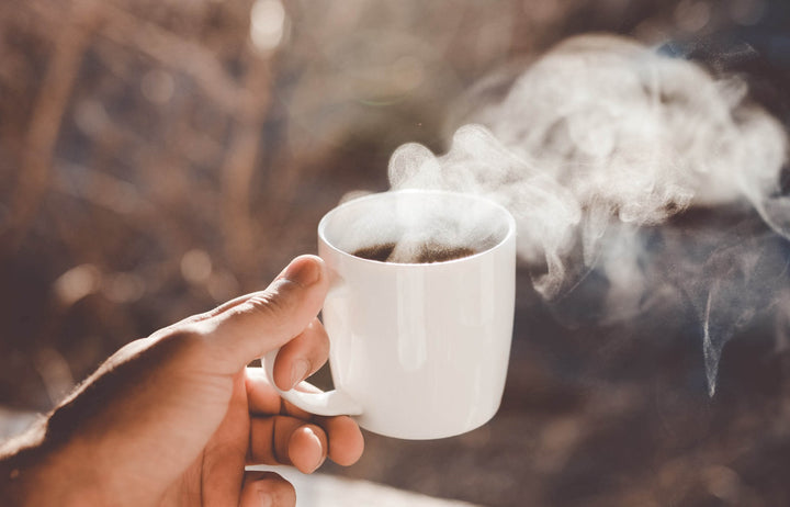 A hand holding a steaming cup of coffee