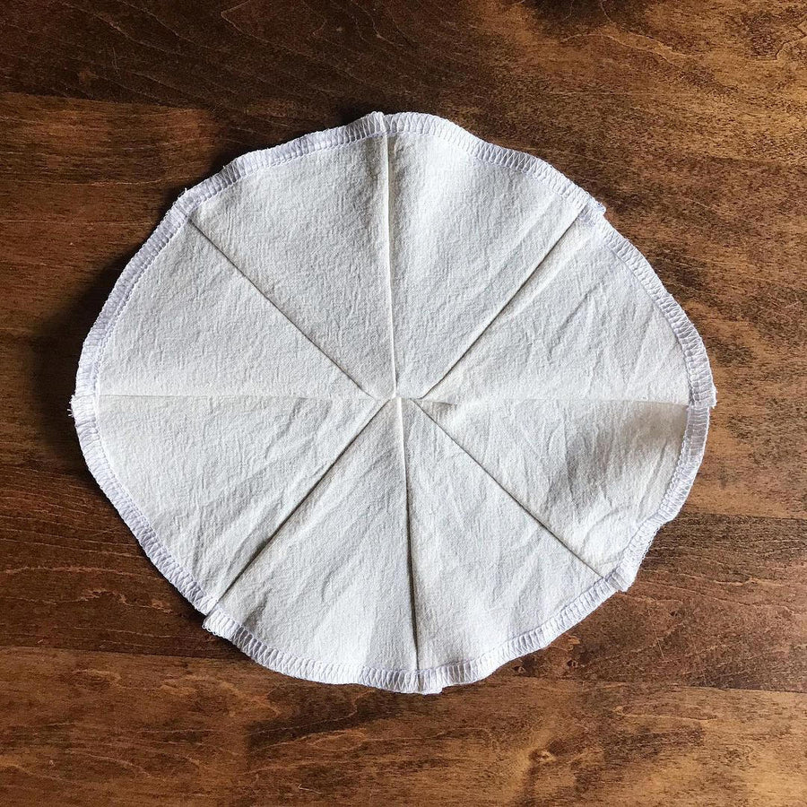A cloth filter is on a wood table. It’s in the shape of a circle and has 4 seams running through it.
