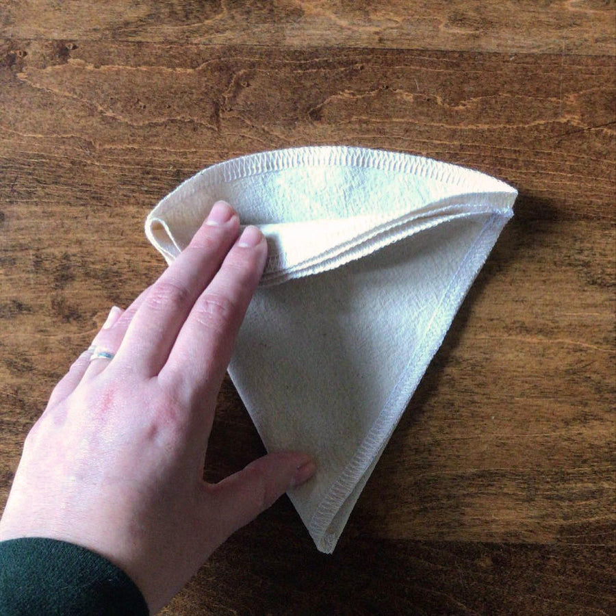 A cloth filter is being held open to show the pocket for grinds and the 3 layers of cloth.